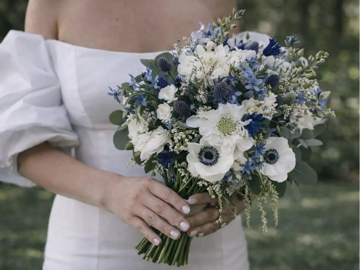 Buquê com flores claras e detalhes em tons profundos segurado pela noiva.