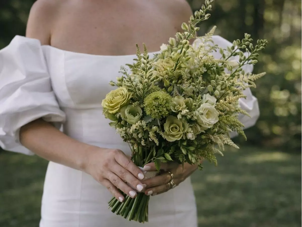 Buquê de flores em tons claros e esverdeados segurado pela noiva.