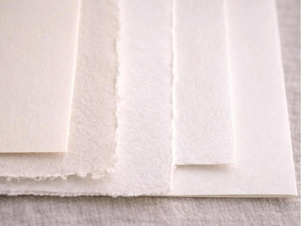 Detalhe de diferentes papéis claros empilhados, mostrando textura e acabamento.