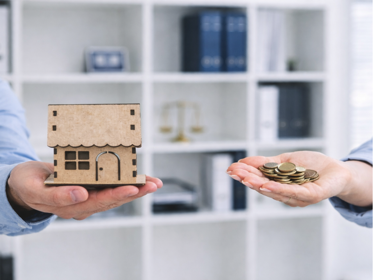 Pessoa segurando uma miniatura de casa em uma mão e moedas na outra, simbolizando divisão e apuração de patrimônio.