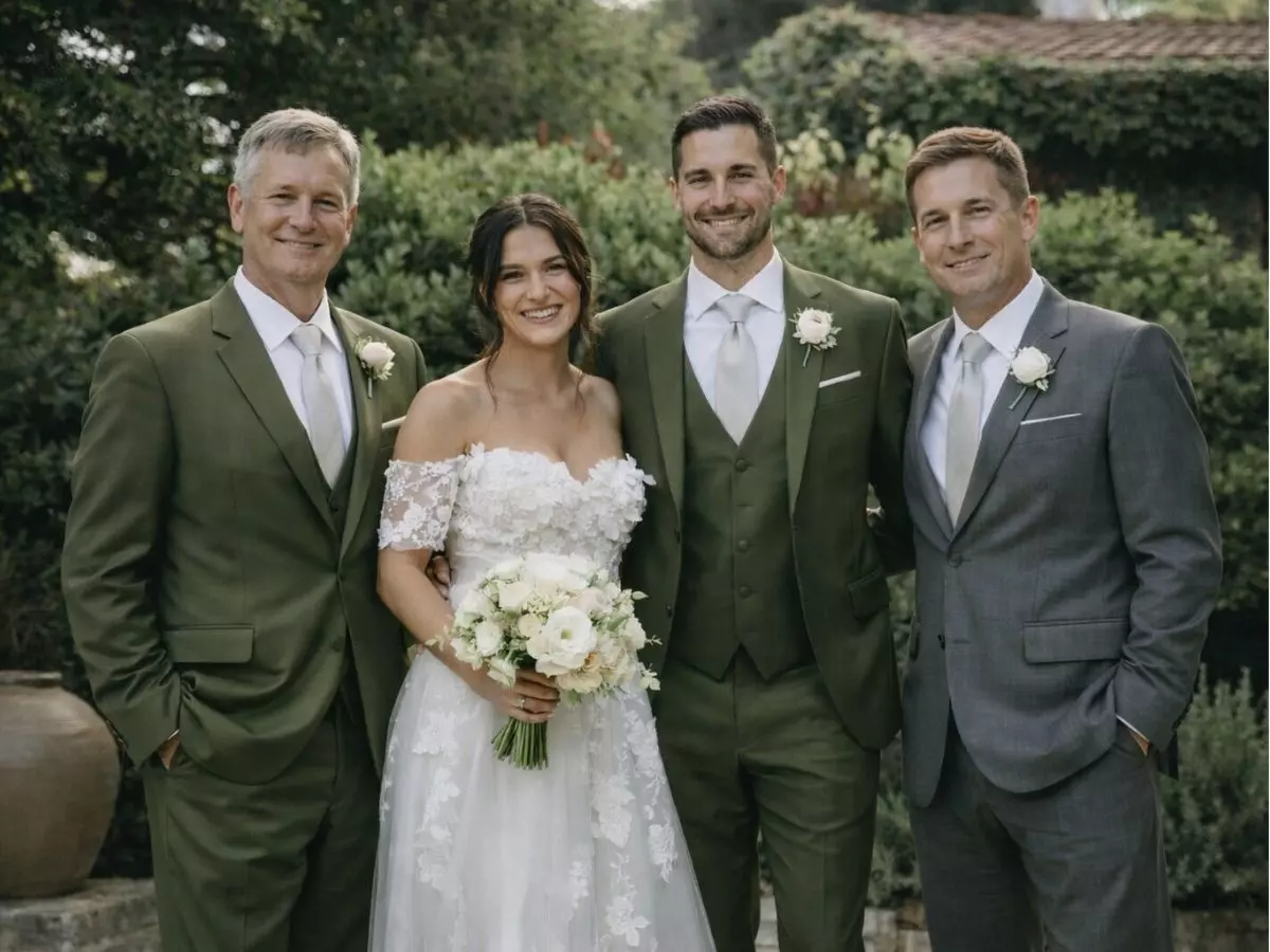 Casal recém-casado ao lado dos pais, todos sorrindo em ambiente externo decorado.