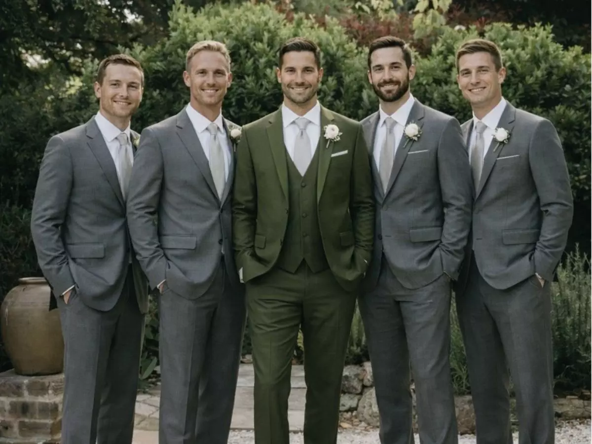 Homens em trajes formais alinhados ao redor do noivo, em cenário ao ar livre com vegetação ao fundo.