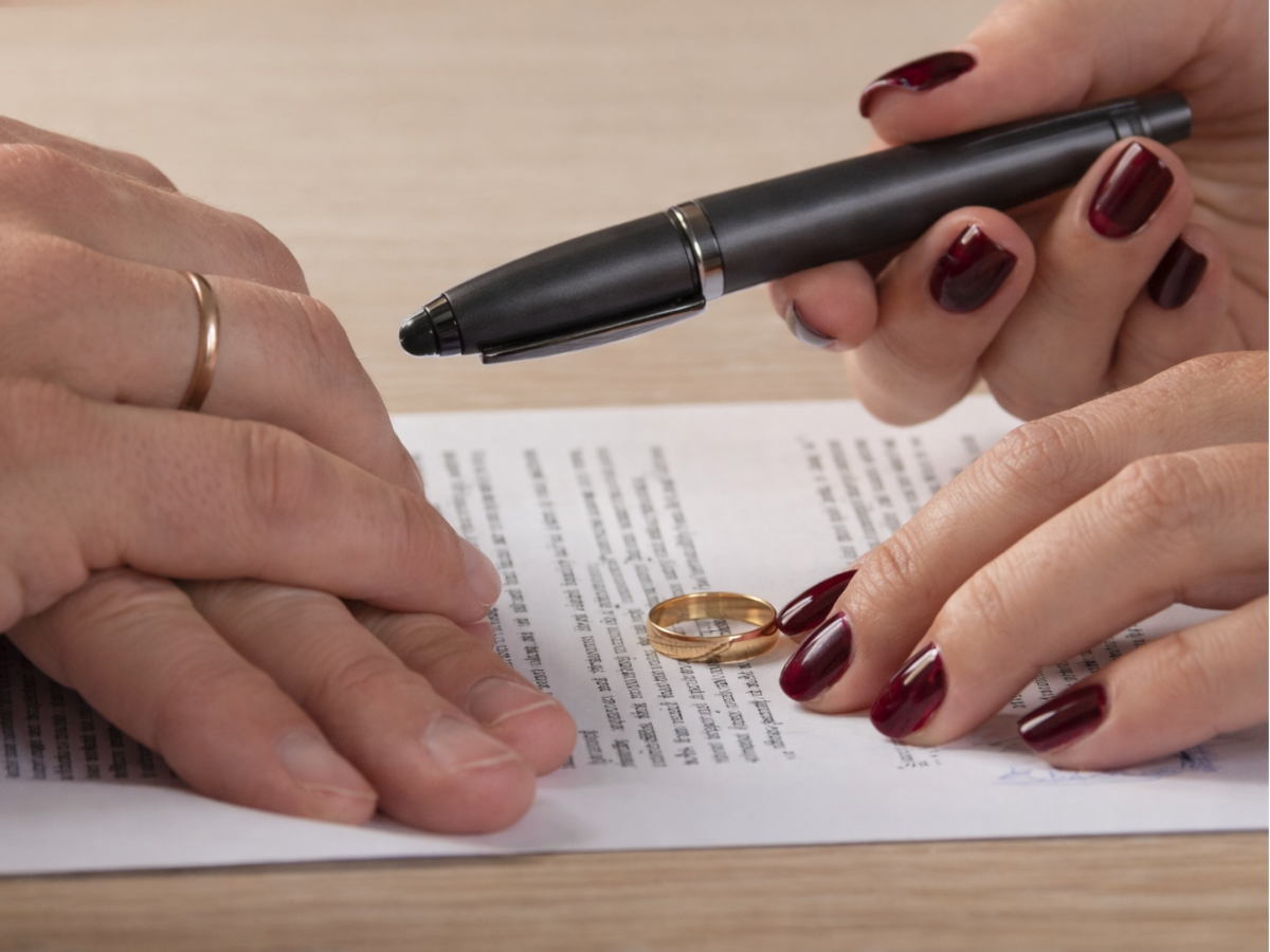 Mãos de duas pessoas analisando um documento, com caneta em destaque e aliança apoiada sobre o papel.