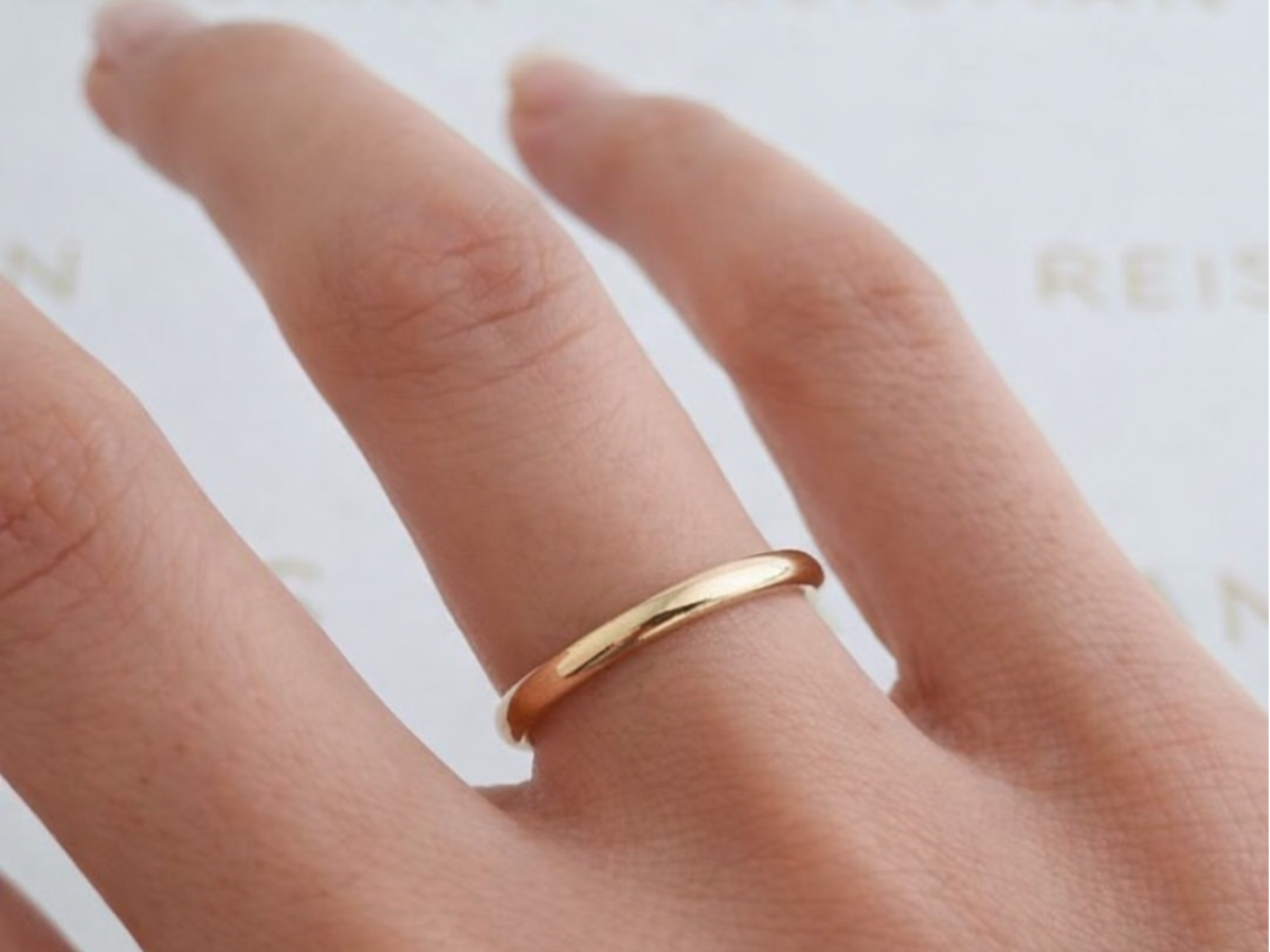 Aliança lisa de ouro tradicional no dedo em fundo neutro.