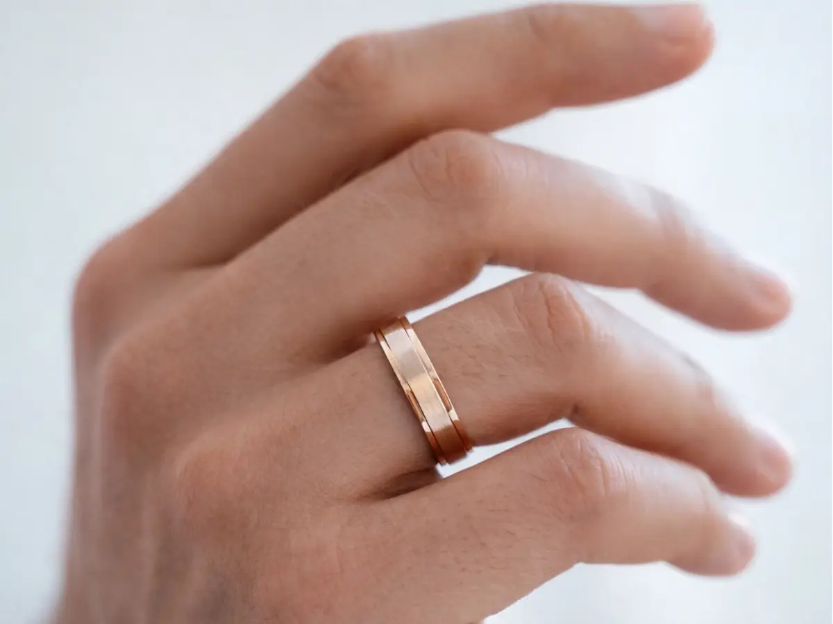 Aliança masculina de ouro com acabamento fosco no dedo.