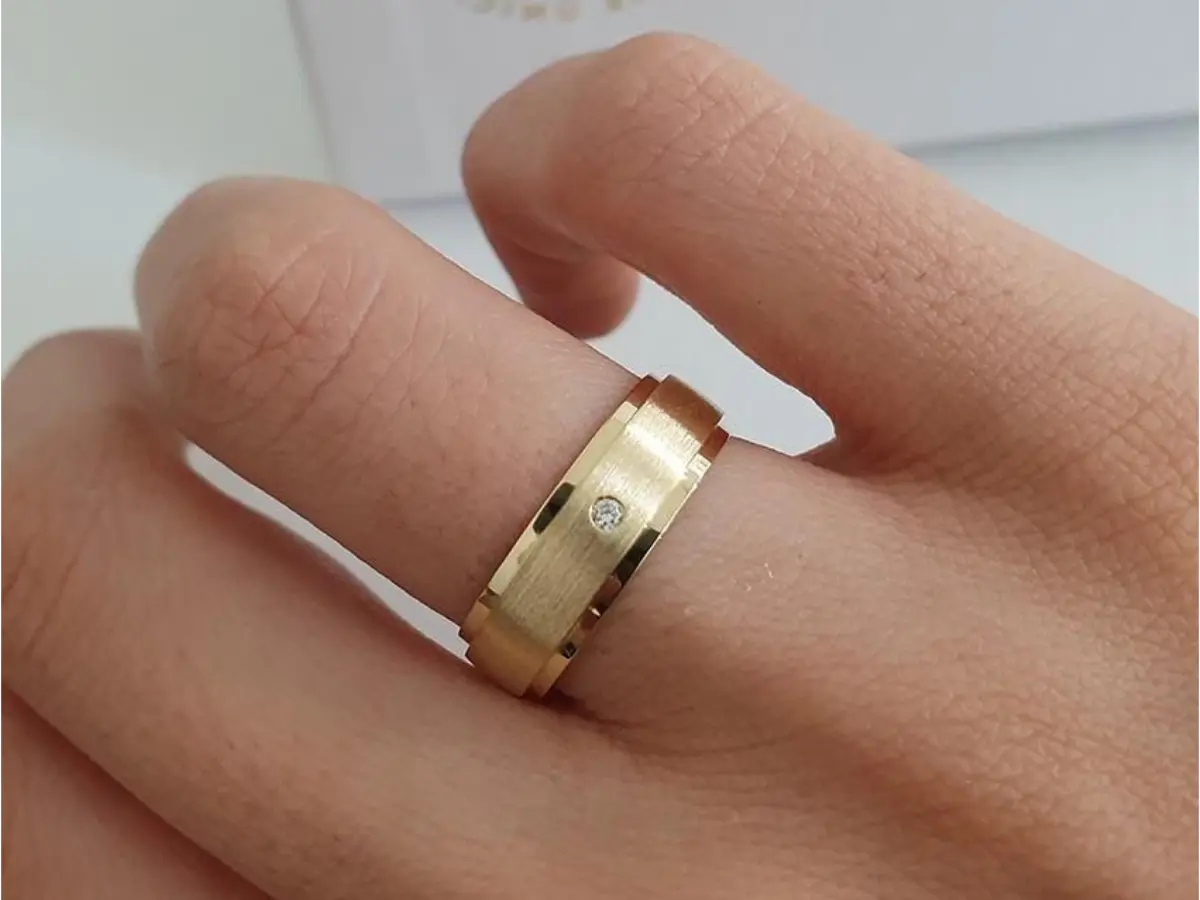 Aliança moderna de ouro com pequeno diamante central no dedo.
