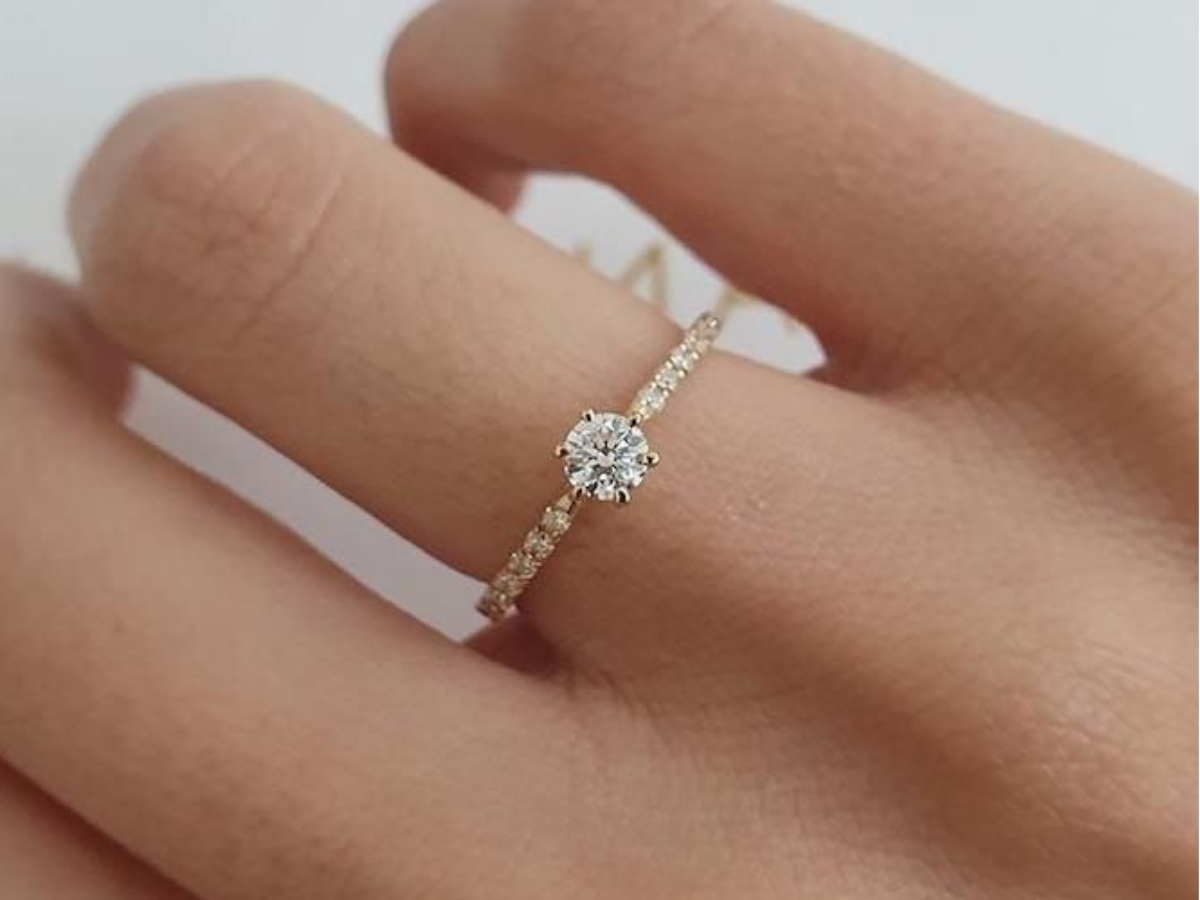 Anel solitário com diamante delicado no dedo, em close.