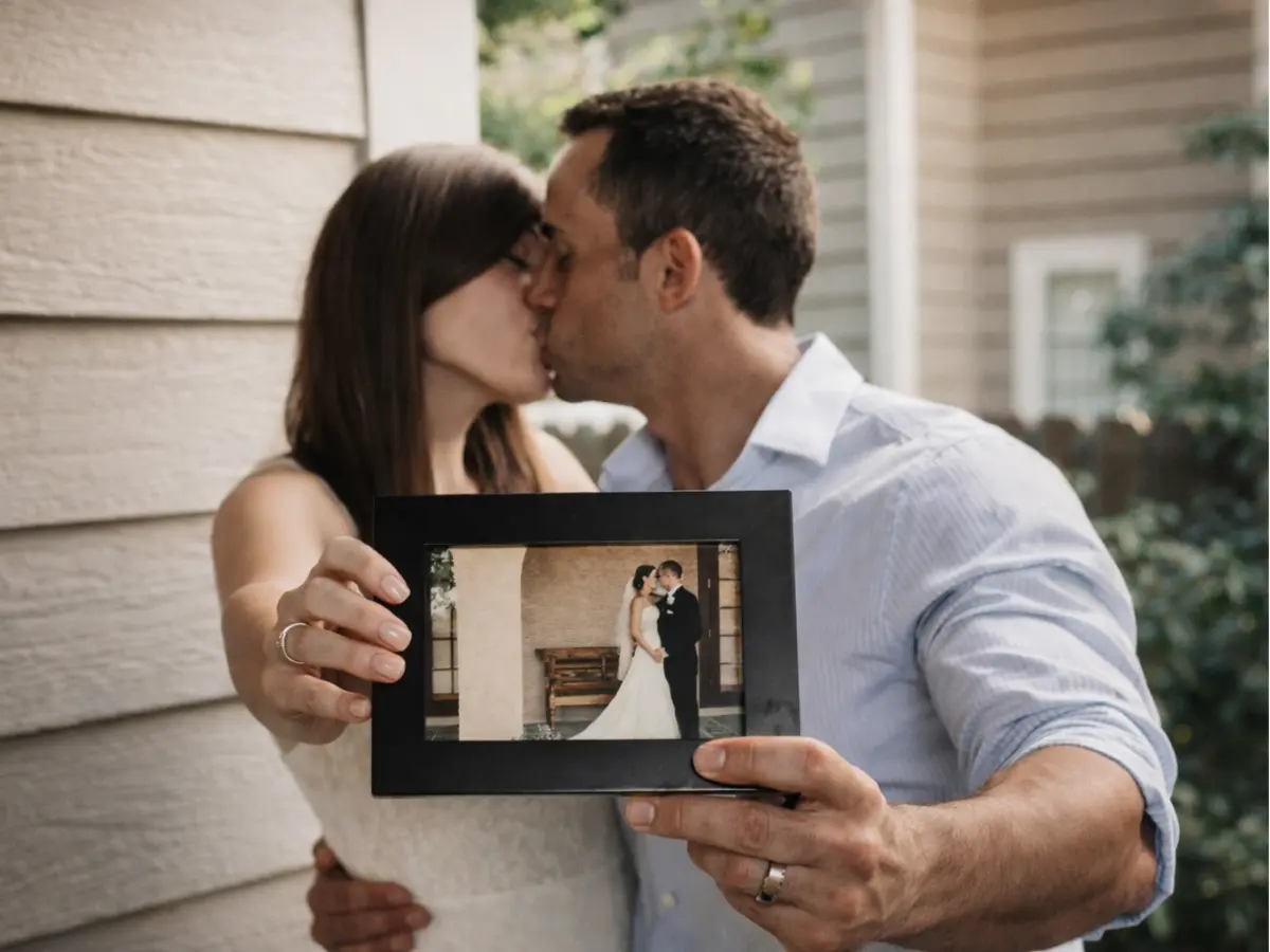 Casal se beijando enquanto segura foto antiga do dia da cerimônia