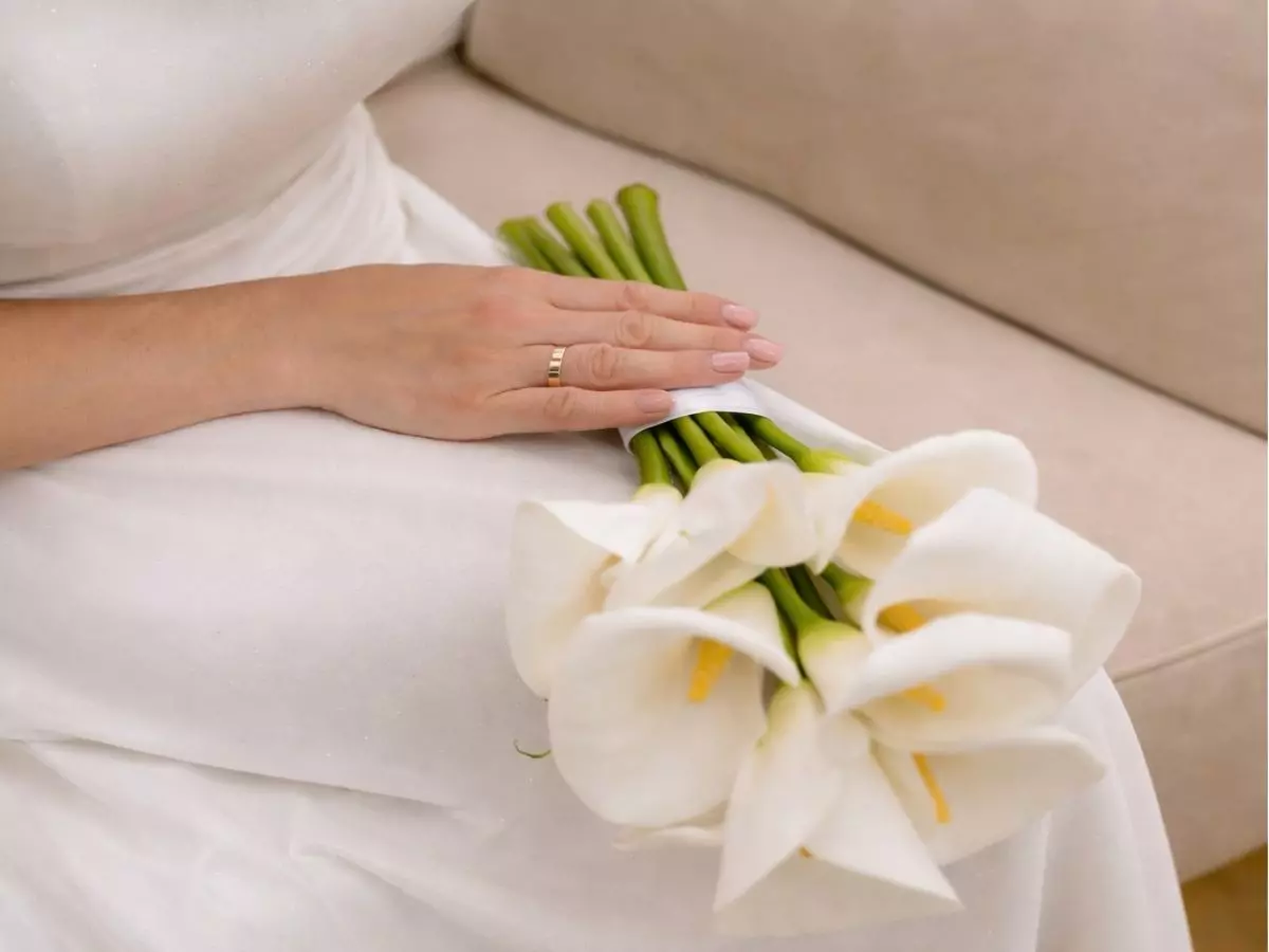 Buquê de copos-de-leite brancos apoiado no colo da noiva com vestido claro