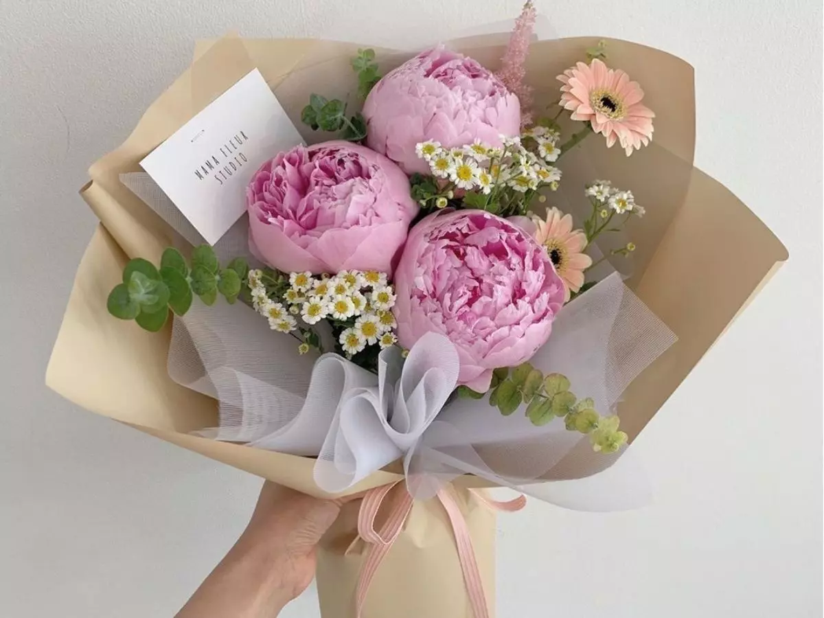 Buquê de peônias rosas com flores delicadas e folhagens verdes em embalagem bege