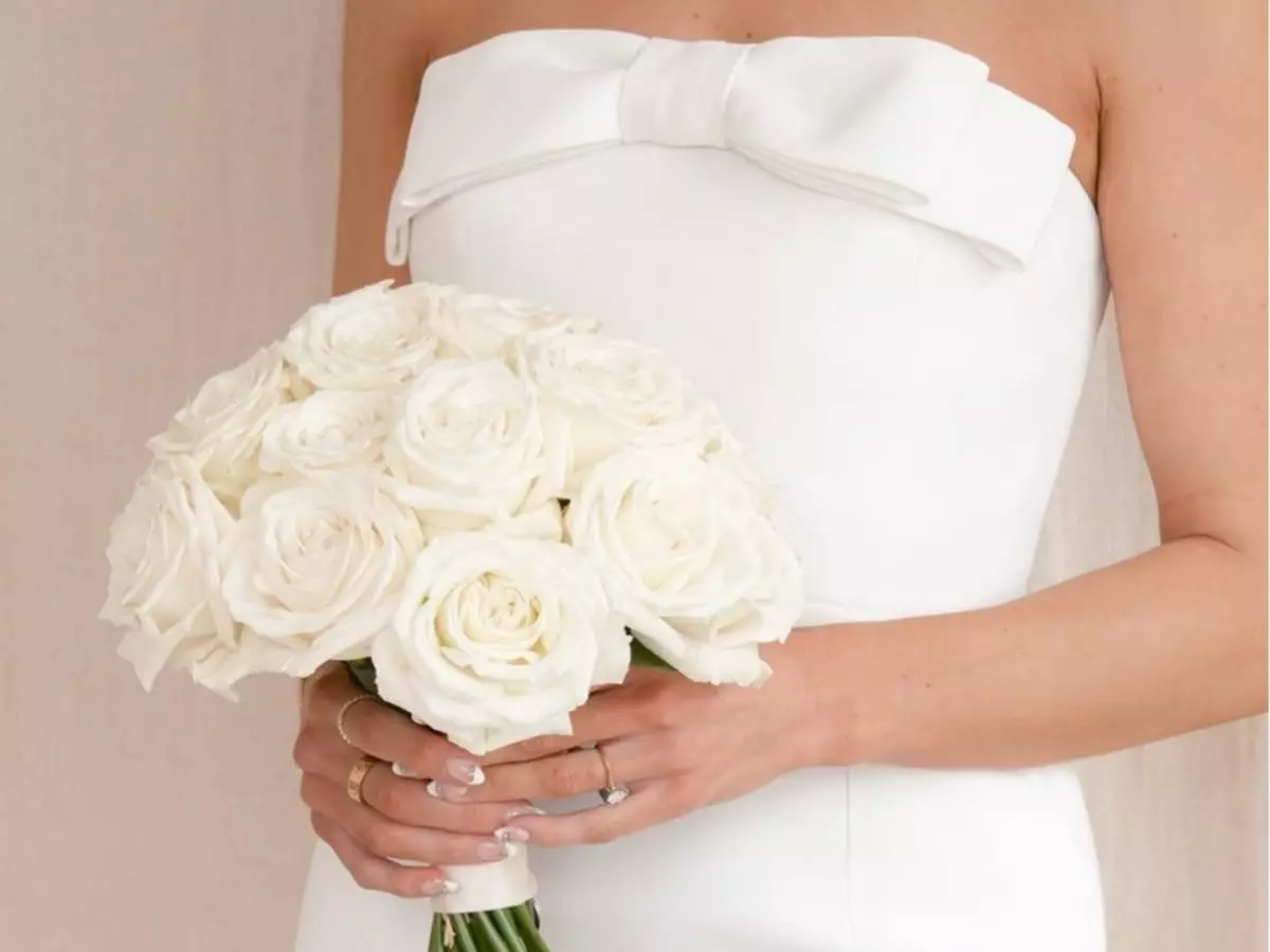 Buquê de rosas brancas em formato clássico segurado por noiva com vestido tomara que caia