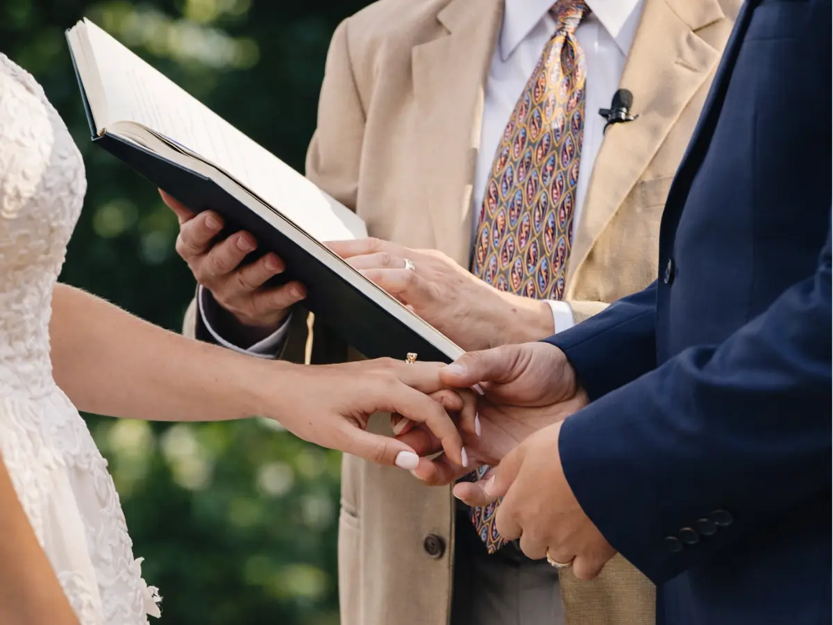 Mãos dos noivos durante a a leitura dos votos pele celebrante na cerimônia de casamento ao ar livre