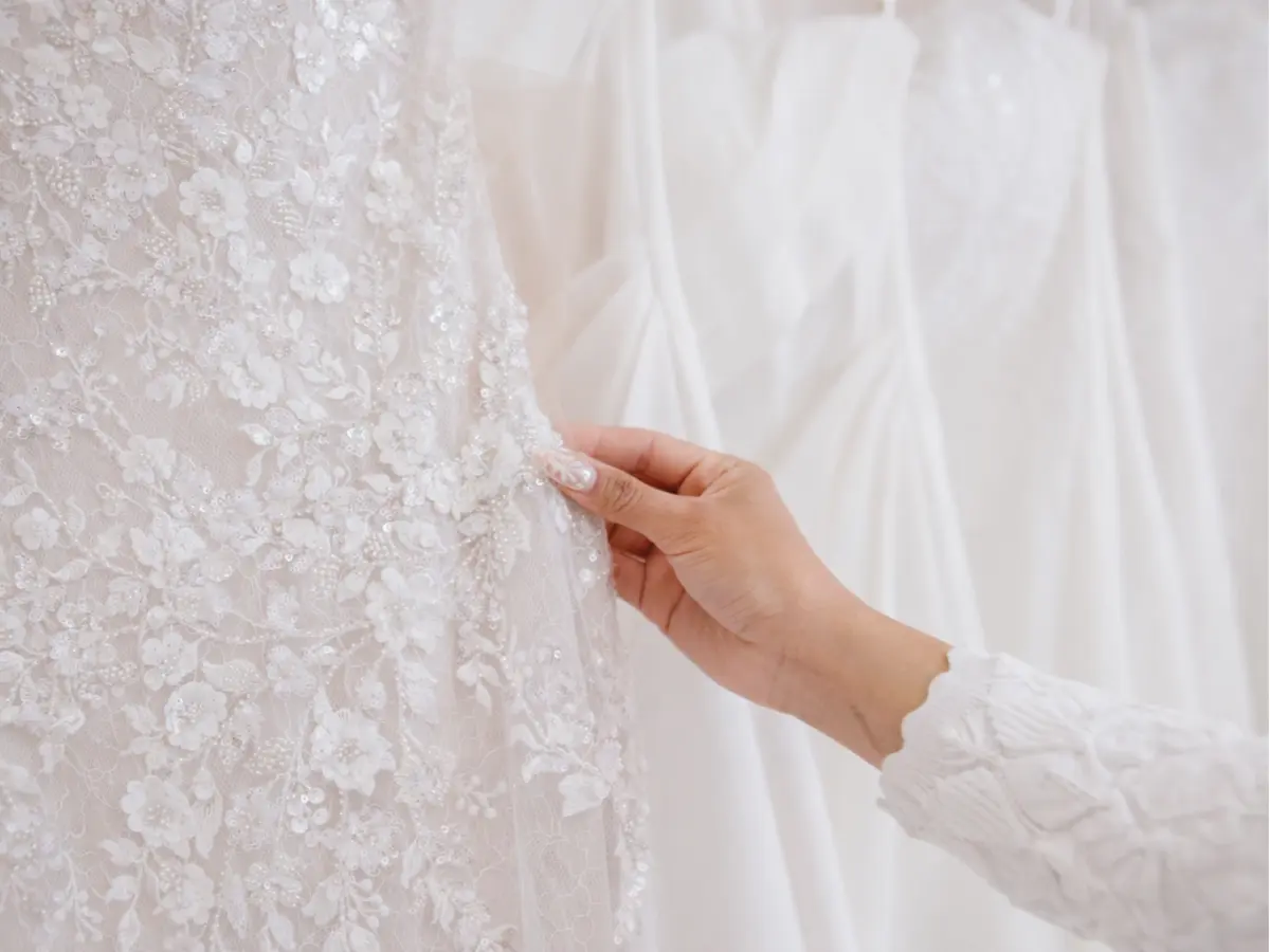 Detalhe tecidos de renda e bordado em vestido de noiva sendo escolhido à mão
