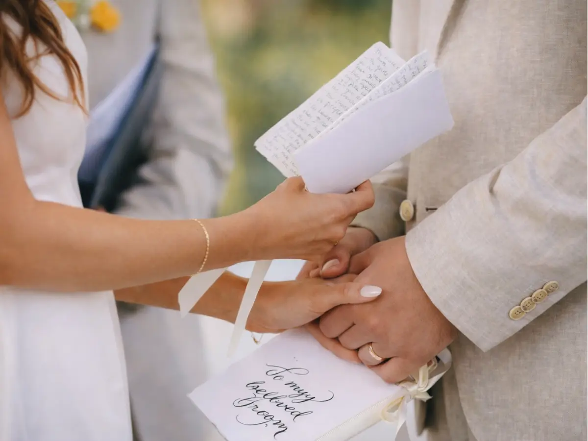 Noiva lendo votos de casamento enquanto segura a mão do noivo durante a cerimônia