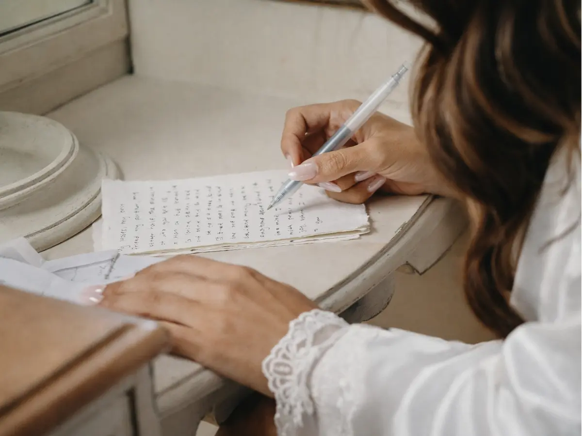 Detalhe das mãos da noiva escrevendo votos de casamento simples à mão