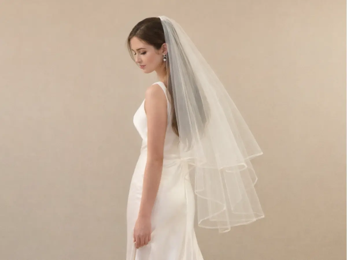 Noiva usando véu longo na altura da ponta dos dedos.